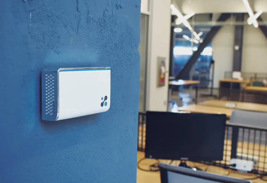 Aethair IAQ air quality monitor mounted on a concrete wall inside a modern workspace.