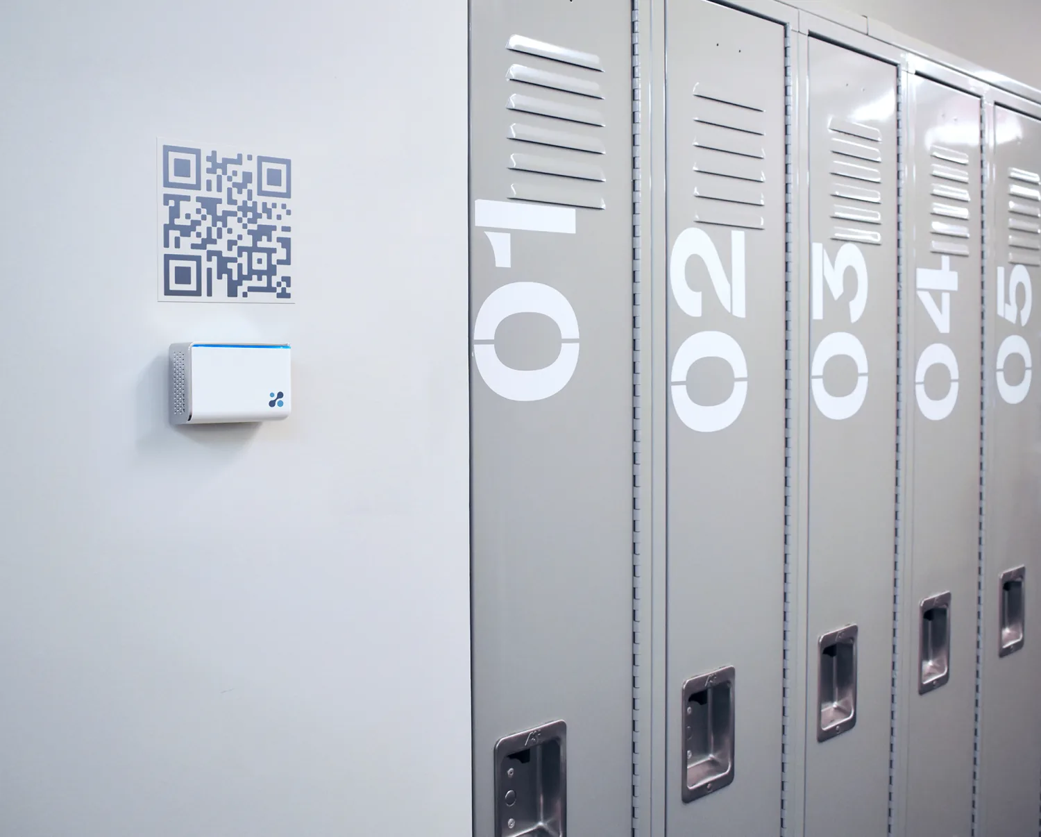 Aethair IAQ on a school hallway wall beside the lockers, a QR code sign above it.