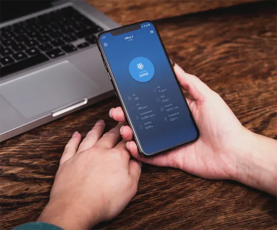 Man using the Aethair mobile app on a smartphone held above a wooden table with a laptop in the background.