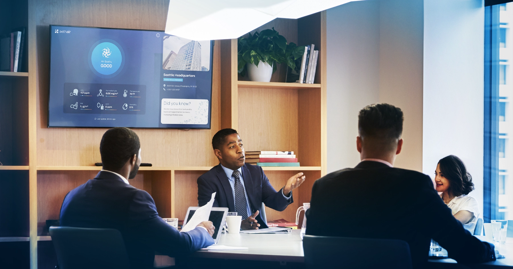 Conference room meeting with Aethair Dashboard air quality display visible on tv in background.