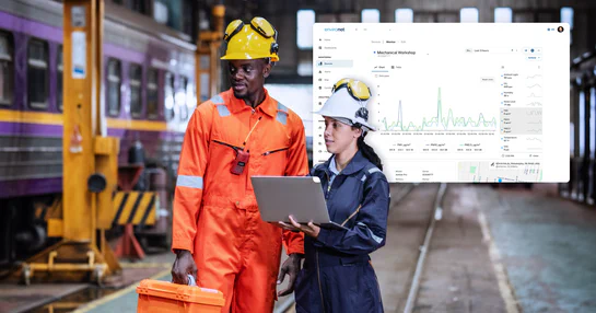 Two industrial workers reviewing real-time particulate matter data on a laptop with an Environet dashboard displayed behind them.