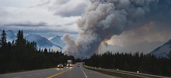Smoke plume drifting over a forested landscape with an Aethair PRO air quality monitor in the foreground reporting real-time PM2.5 readings