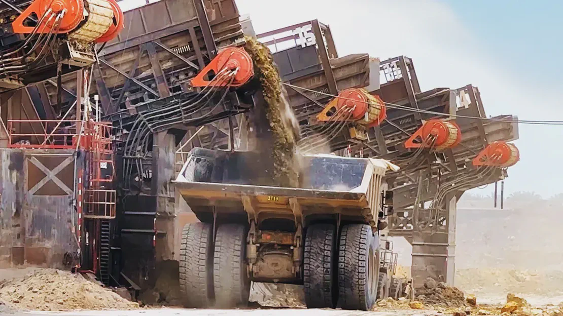 Mining equipment dumping dirt into a large dump truck.