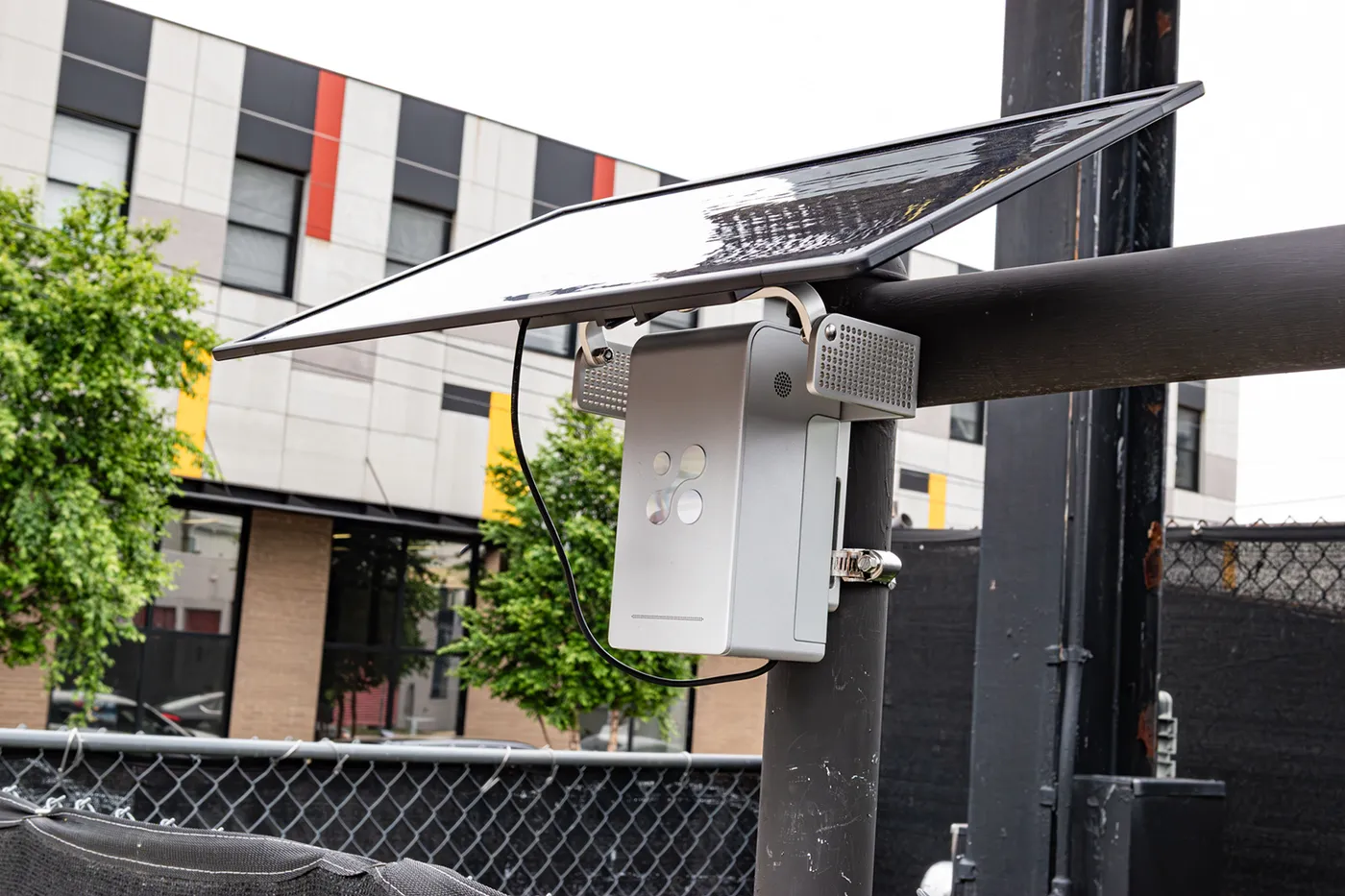 Aethair PRO under its solar panel on a metal pole by a chain-link fence, running off-grid.