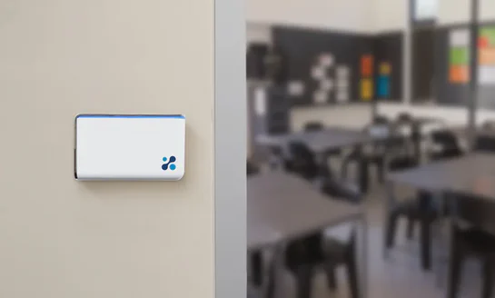An Aethair IAQ air quality monitor mounted beside a school classroom doorway.
