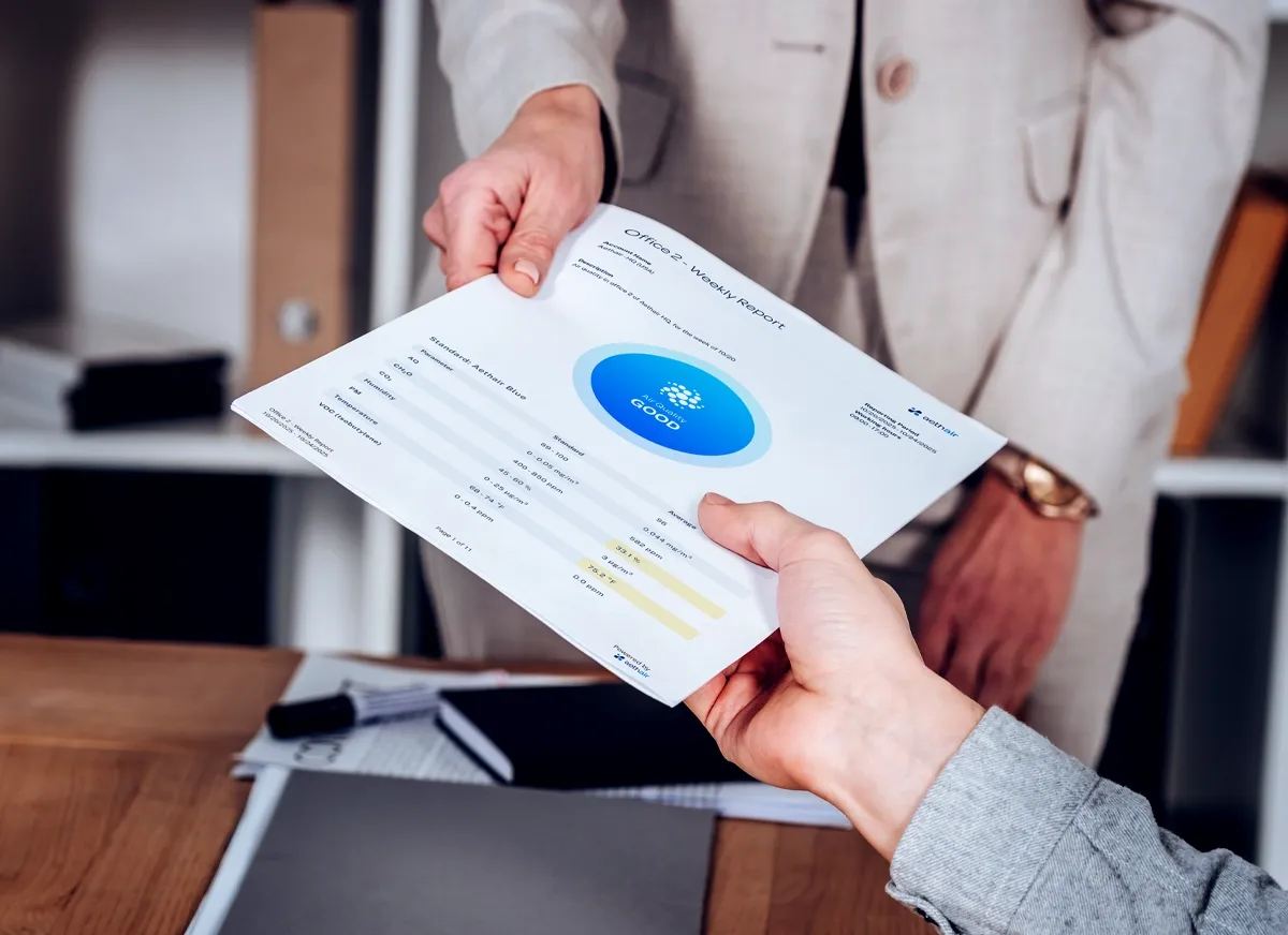 Hands passing a printed Aethair air quality report across a desk.