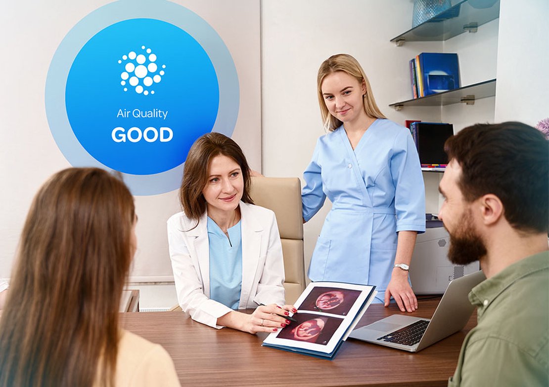 Doctor showing new parents ultrasound images with Aethair “Good” air quality status displayed behind her.