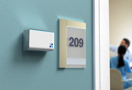 Aethair IAQ mounted next to a room number in a hallway with doctors talking in the background.