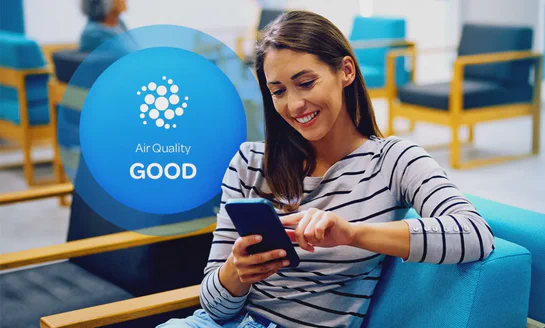 Aethair “Good” air quality status displayed behind a woman checking air quality data on her phone.