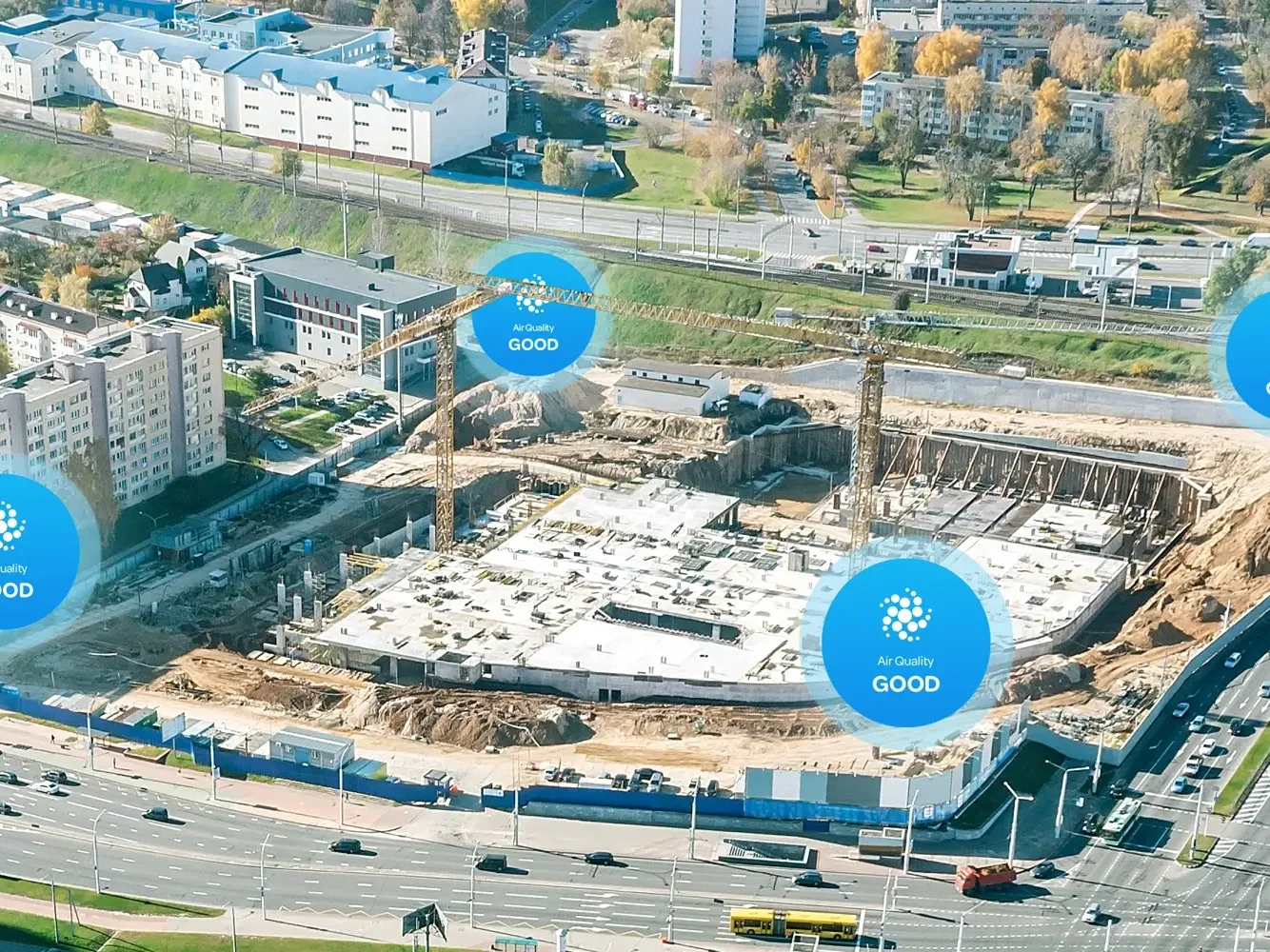 Aerial view of a city construction site with air quality monitors at its boundary, each showing an "Air Quality GOOD" status.
